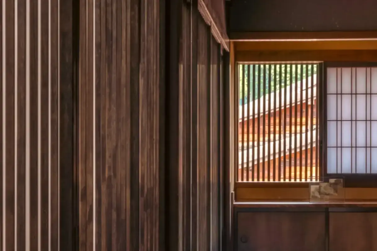 Modern Japanese-inspired interior featuring vertical wood slat walls and a window with decorative lattice screen filtering natural light, alongside traditional shoji screen panels.
