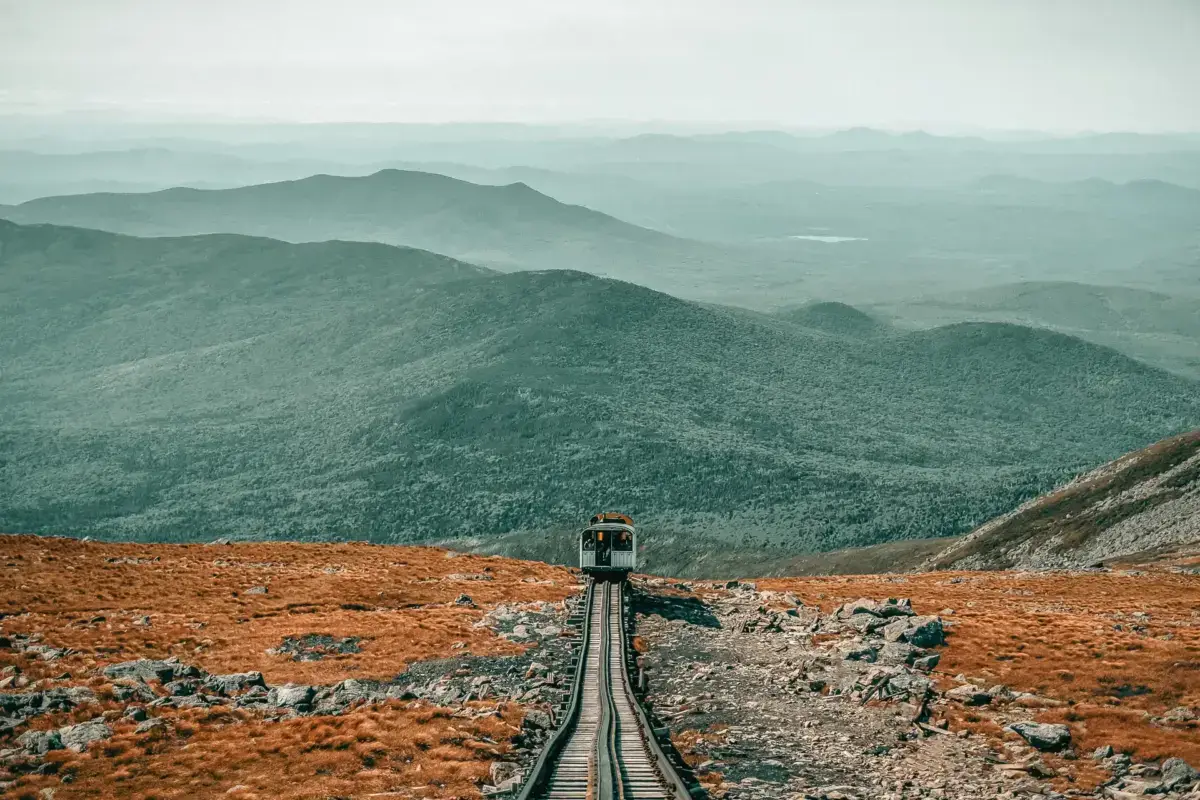 Mountain railway cog train ascending steep tracks through rocky terrain with misty layered mountain ranges in the background, illustrating sustainable transportation for eco-conscious travel.