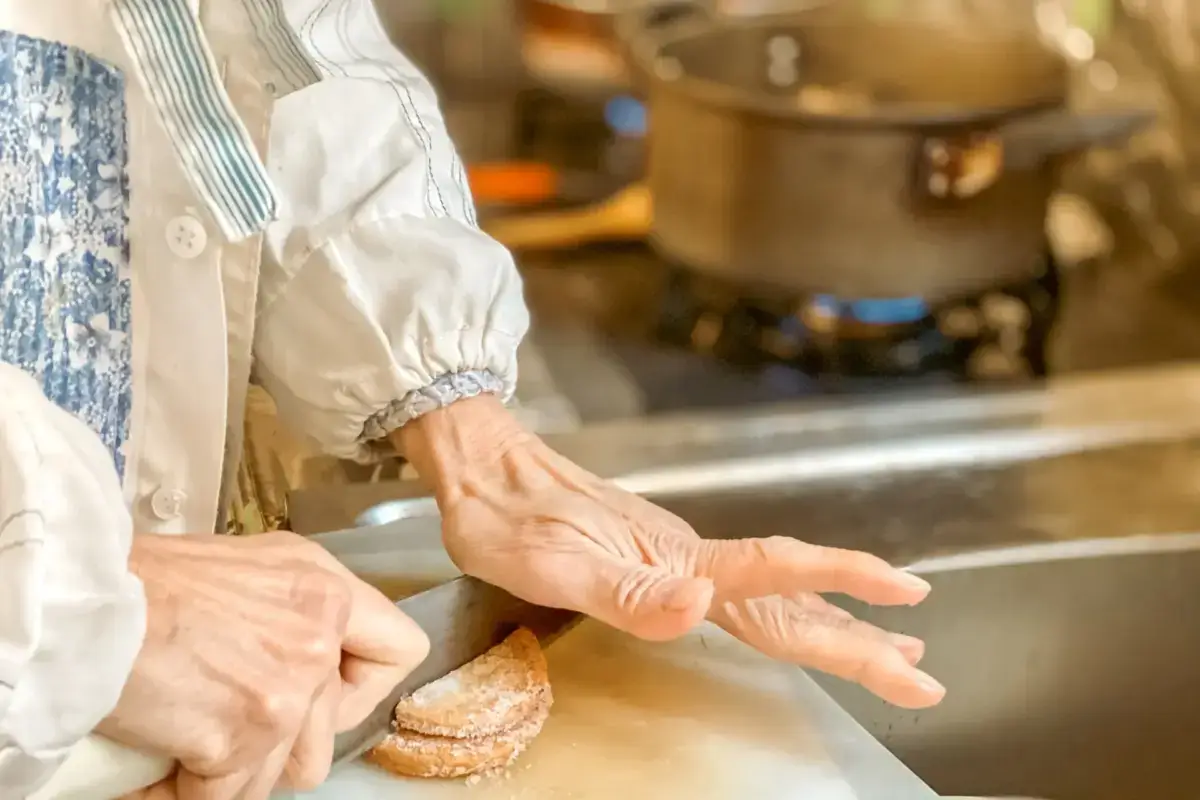 Person in traditional Japanese apron preparing homemade cookies in a kitchen, dusting powdered sugar over freshly baked round cookies with a pot on the stove in the background.