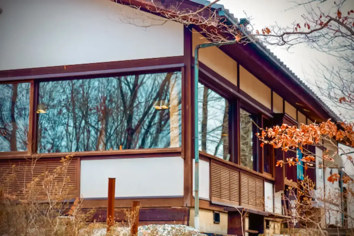 Traditional Japanese building with dark wooden frames, large windows, and tiled roof surrounded by autumn foliage and bare winter branches, showcasing sustainable community architecture.