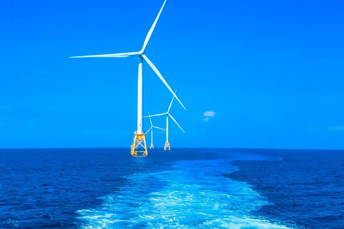 Offshore wind turbines with white blades and yellow foundations standing in deep blue ocean waters under a clear sky, representing renewable energy infrastructure for the blue economy.
