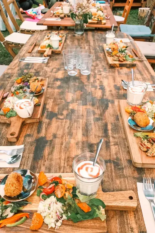 Rustic wooden dining table set with colorful healthy meals featuring fresh vegetables, rice, and beverages, arranged for a communal self-care dining experience.