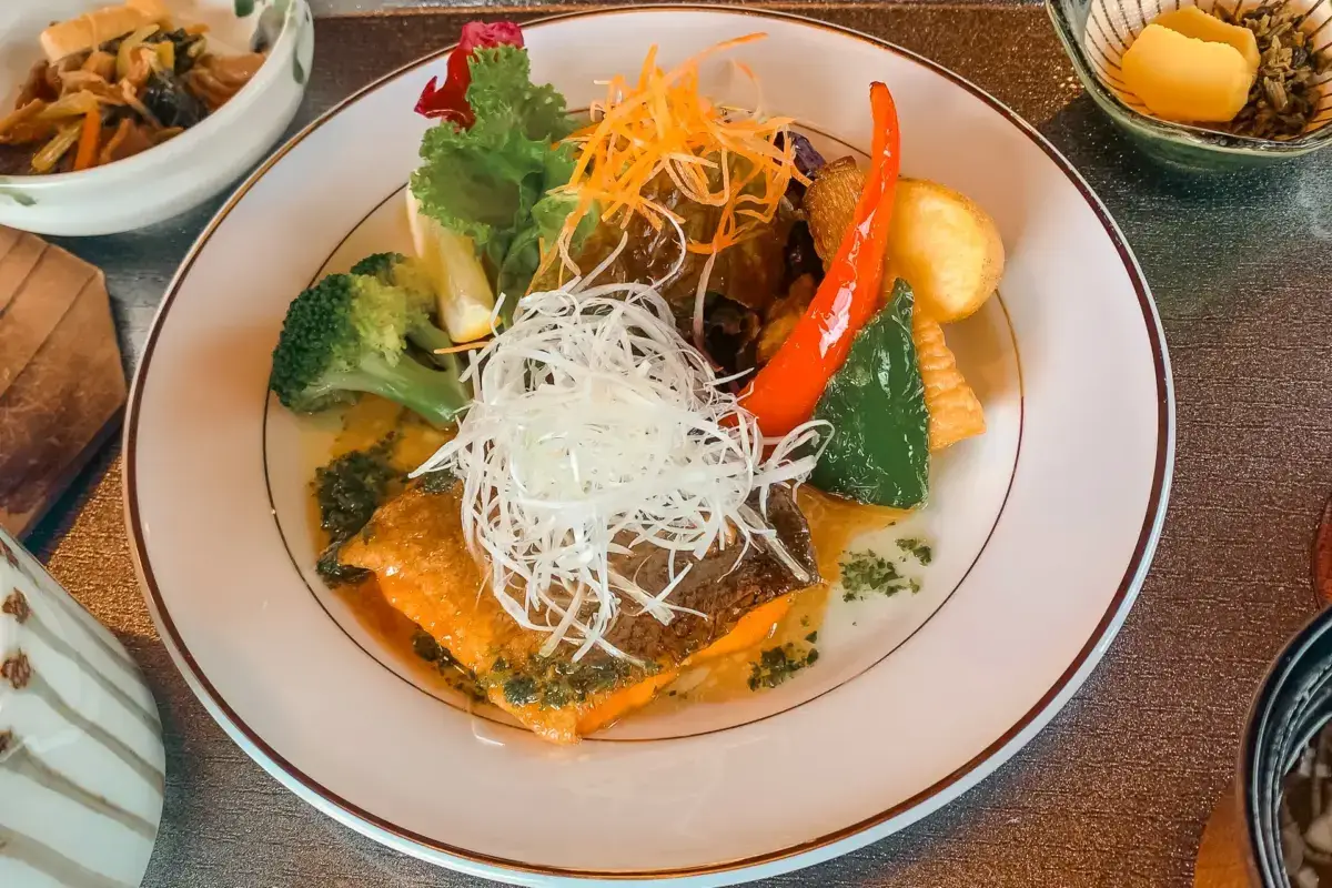 Grilled salmon fillet topped with shredded daikon and carrot, served with steamed broccoli, baby corn, and red bell pepper in a savory sauce.
