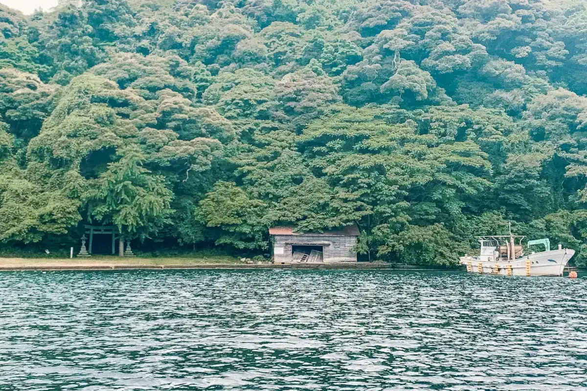 Small wooden fishing boat floating on calm water with dense green forest and mountainside in the background