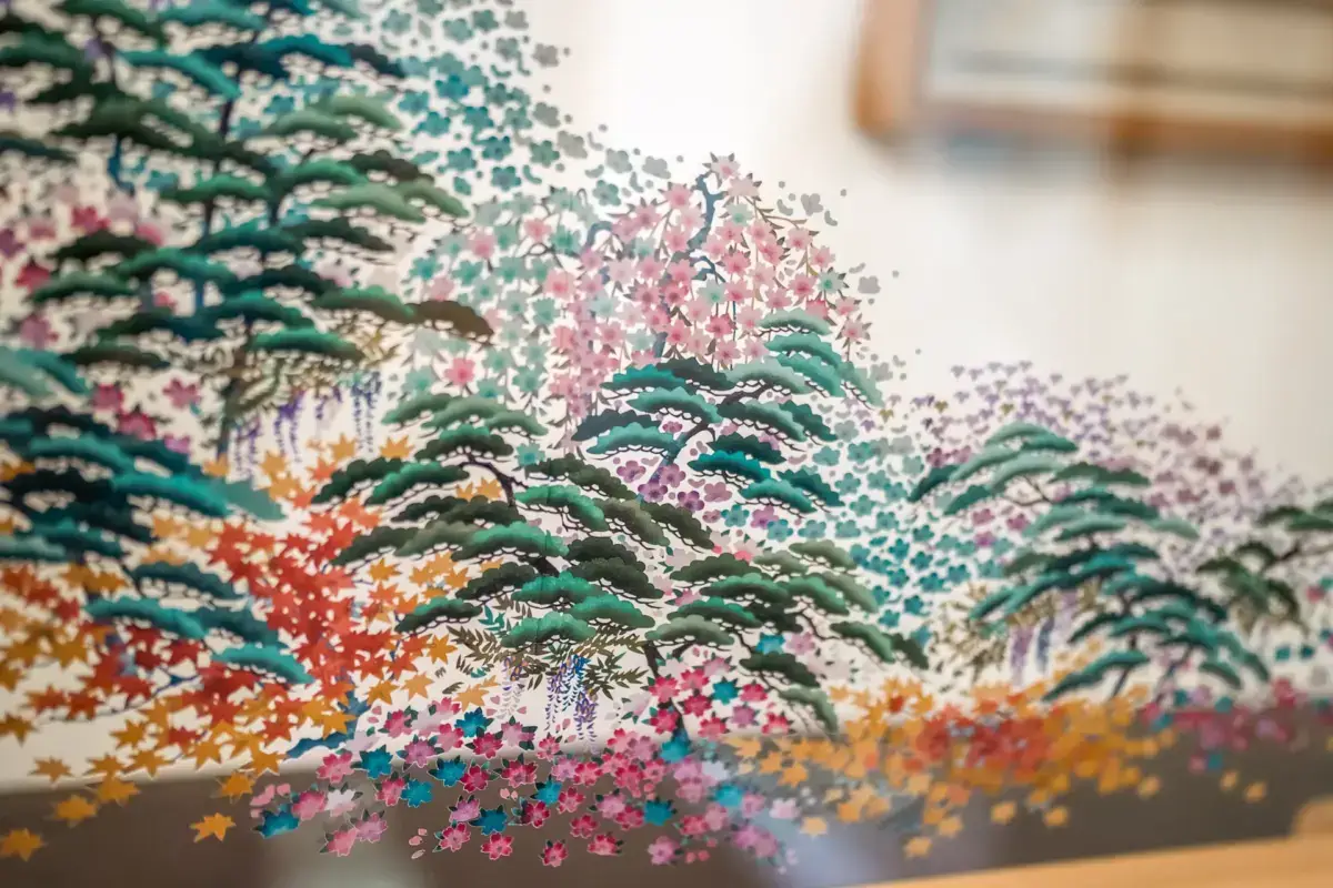 Traditional Japanese art depicting pine trees with colorful seasonal flowers including pink cherry blossoms, orange maple leaves, and purple blooms, painted in a delicate pointillist style on what appears to be decorative paper or screen.