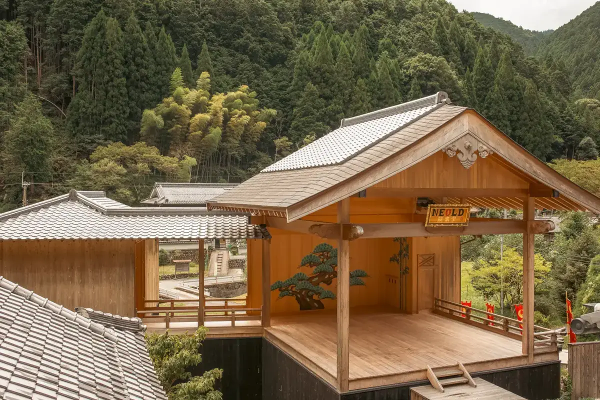 Traditional Japanese wooden building with open deck and covered veranda nestled in lush forested mountains of Yoshino, featuring natural wood construction with tiled roofs.