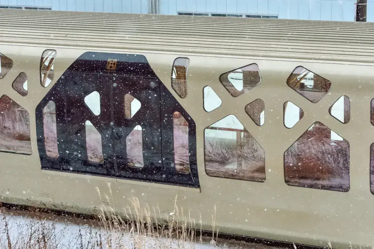 Elegant luxury train exterior with decorative gold and black artistic window panels featuring architectural arch designs, traveling through Japan's countryside.