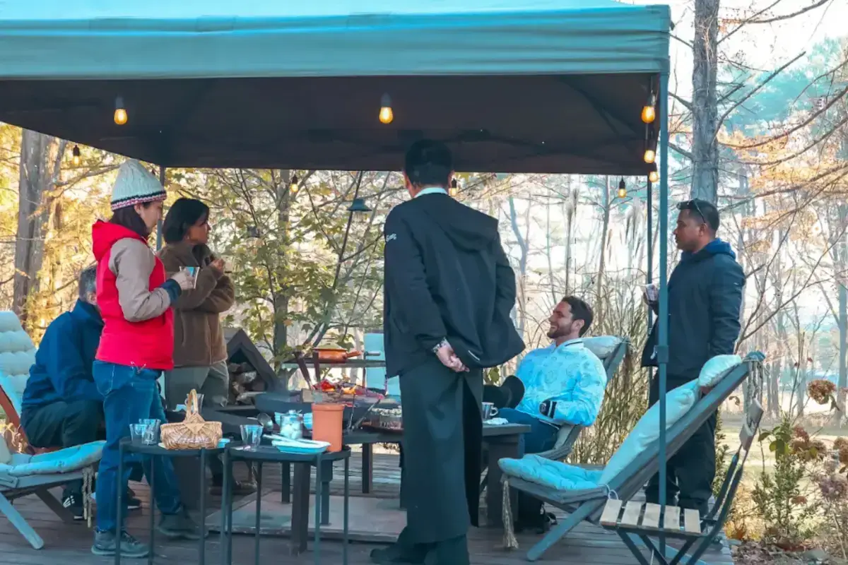 Group of professionals having an outdoor meeting under a blue canopy on a sunny autumn day, with turquoise chairs and trees in the background.