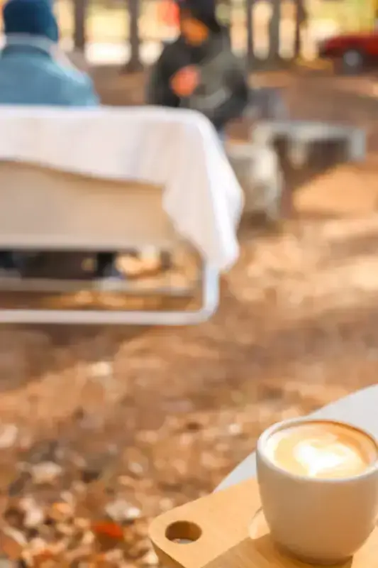 Cappuccino with latte art on wooden table in a casual cafe setting, with blurred people and modern furniture in the background