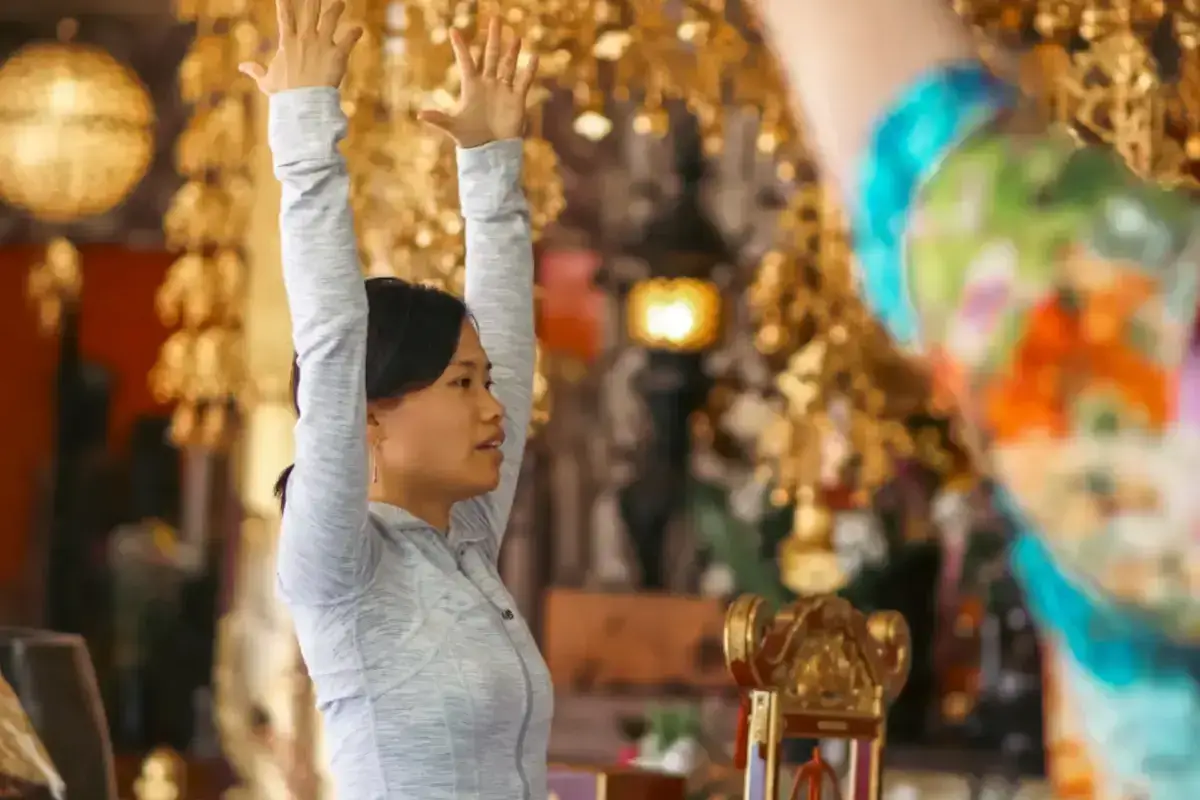 Woman in gray athletic wear stretching with arms raised overhead in a retail store filled with colorful holiday decorations and golden lights.