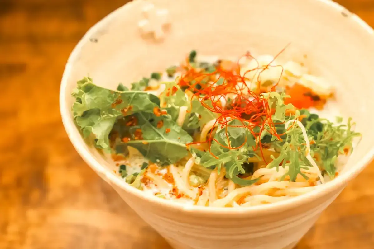 Bowl of noodles topped with fresh lettuce, orange fish roe, and thin red chili pepper garnish on a wooden table