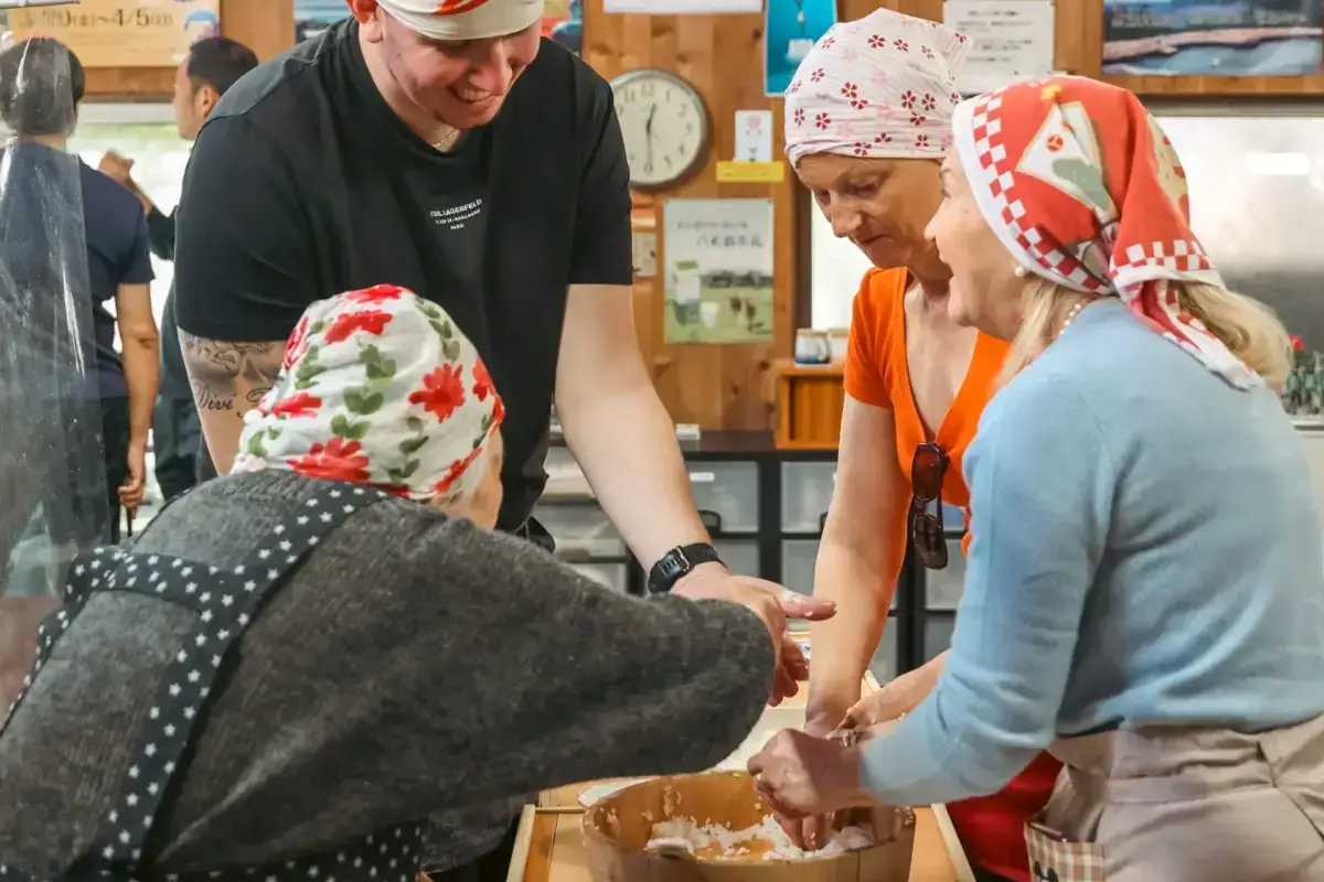 Tourists in colorful traditional Japanese headbands participate in a hands-on mochi-making experience at a local workshop in Hachijojima, guided by an instructor.