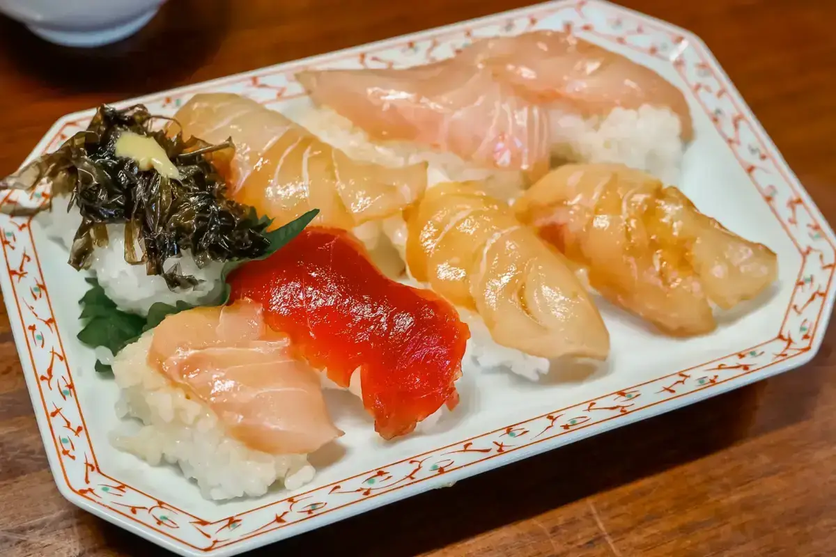 Assorted nigiri sushi platter on decorative plate featuring fresh scallop, salmon, yellowtail, and seaweed garnish from Hachijojima