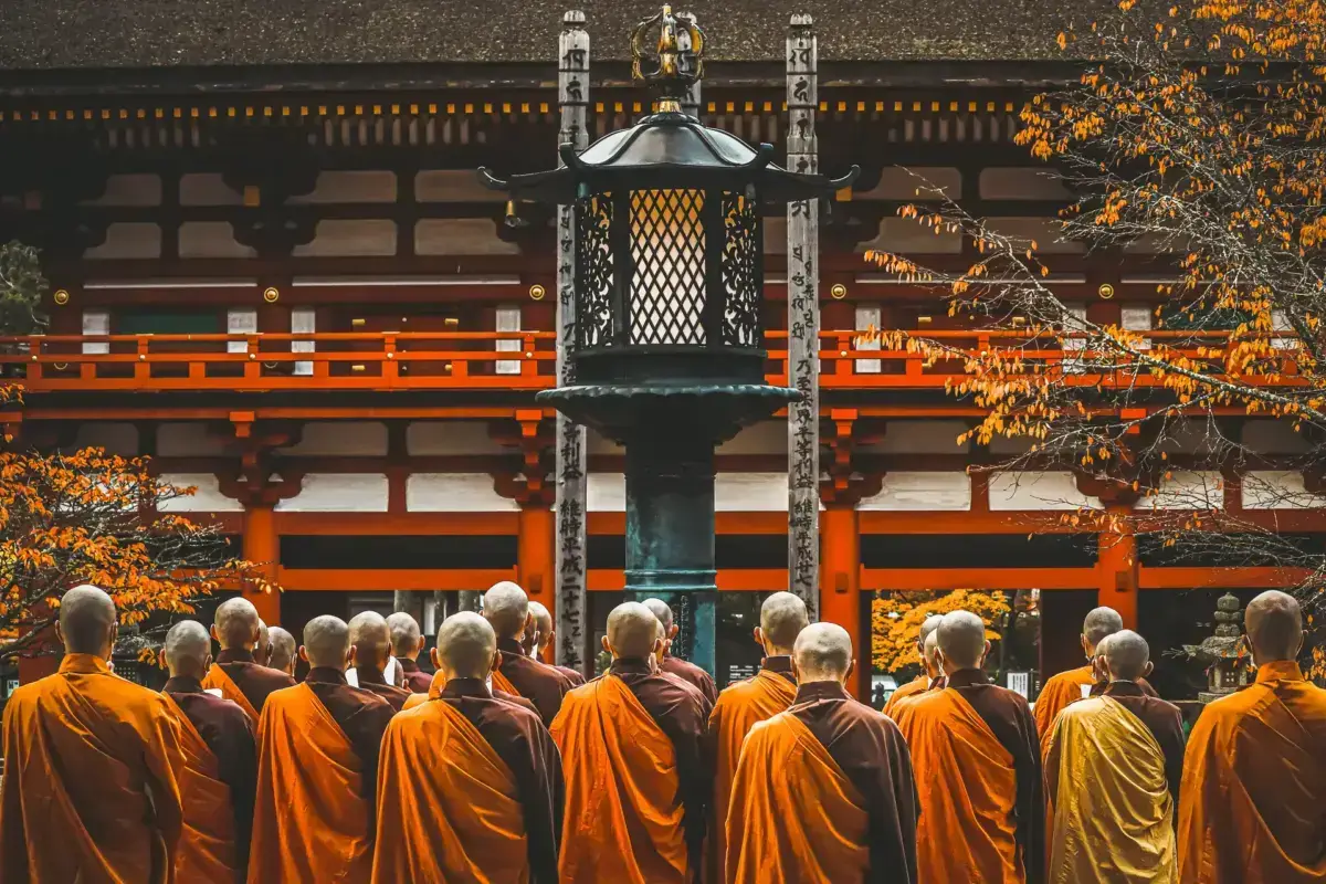Buddhist monks in orange robes gathered before a traditional Japanese temple with ornate lantern and autumn foliage in Wakayama, Japan.