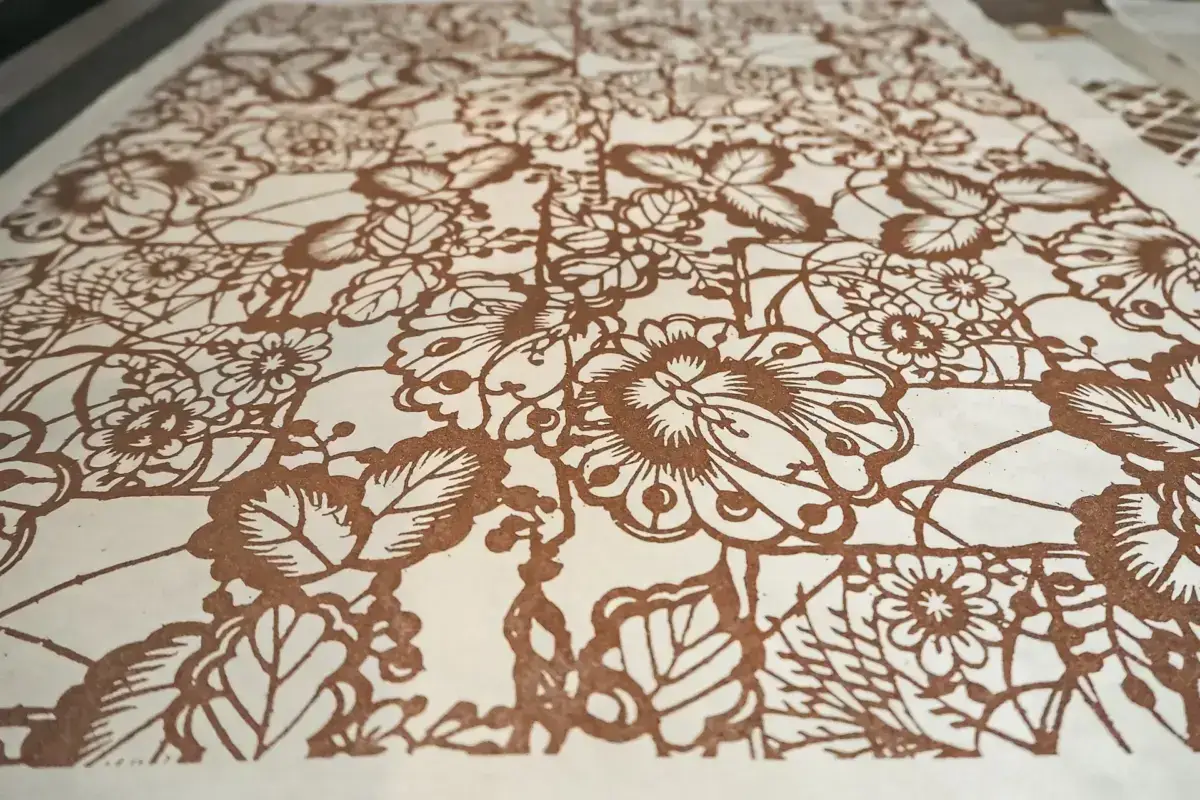 Intricate laser-cut or etched paper artwork featuring elaborate floral and botanical patterns in brown tones on white background.