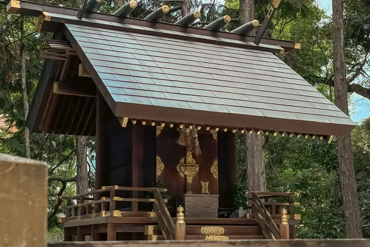 Traditional Japanese shrine with steep thatched roof and ornate golden decorations, surrounded by forest in Aichi Prefecture.