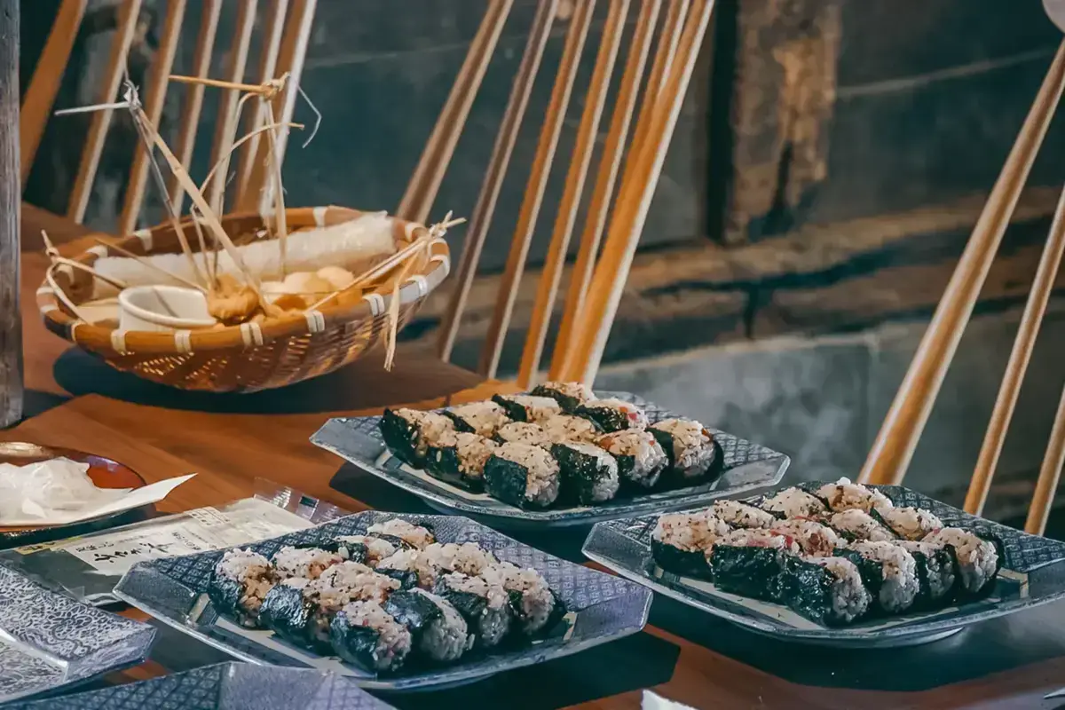 Traditional Japanese onigiri rice balls wrapped in nori seaweed served on blue plates beside a bamboo basket with chopsticks, presented at a riverside dining setting.