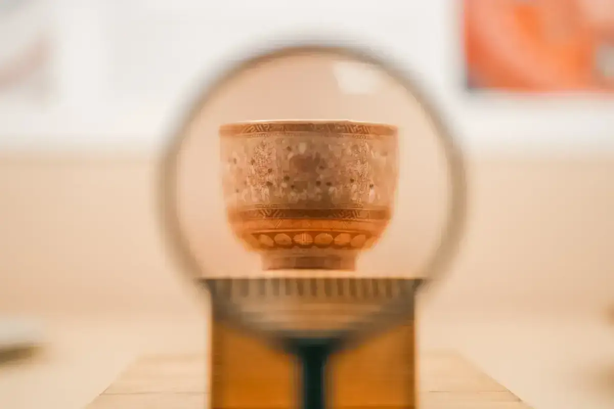 Traditional Japanese teacup with ornate decorative patterns resting on a wooden stand with a circular plate backdrop