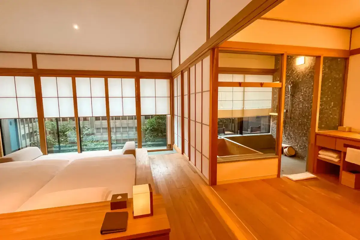 Traditional Japanese ryokan room featuring natural wood flooring, shoji screen doors, and a private hinoki cypress bath overlooking a serene garden courtyard.