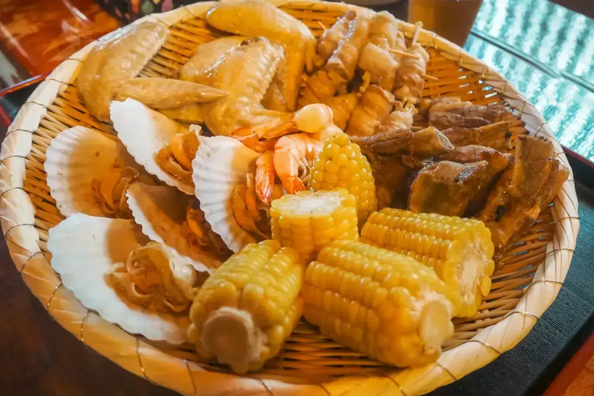 Traditional Japanese bamboo steamer basket filled with assorted steamed seafood including scallops, shrimp, corn on the cob, and various mushrooms, showcasing local Kyushu cuisine.