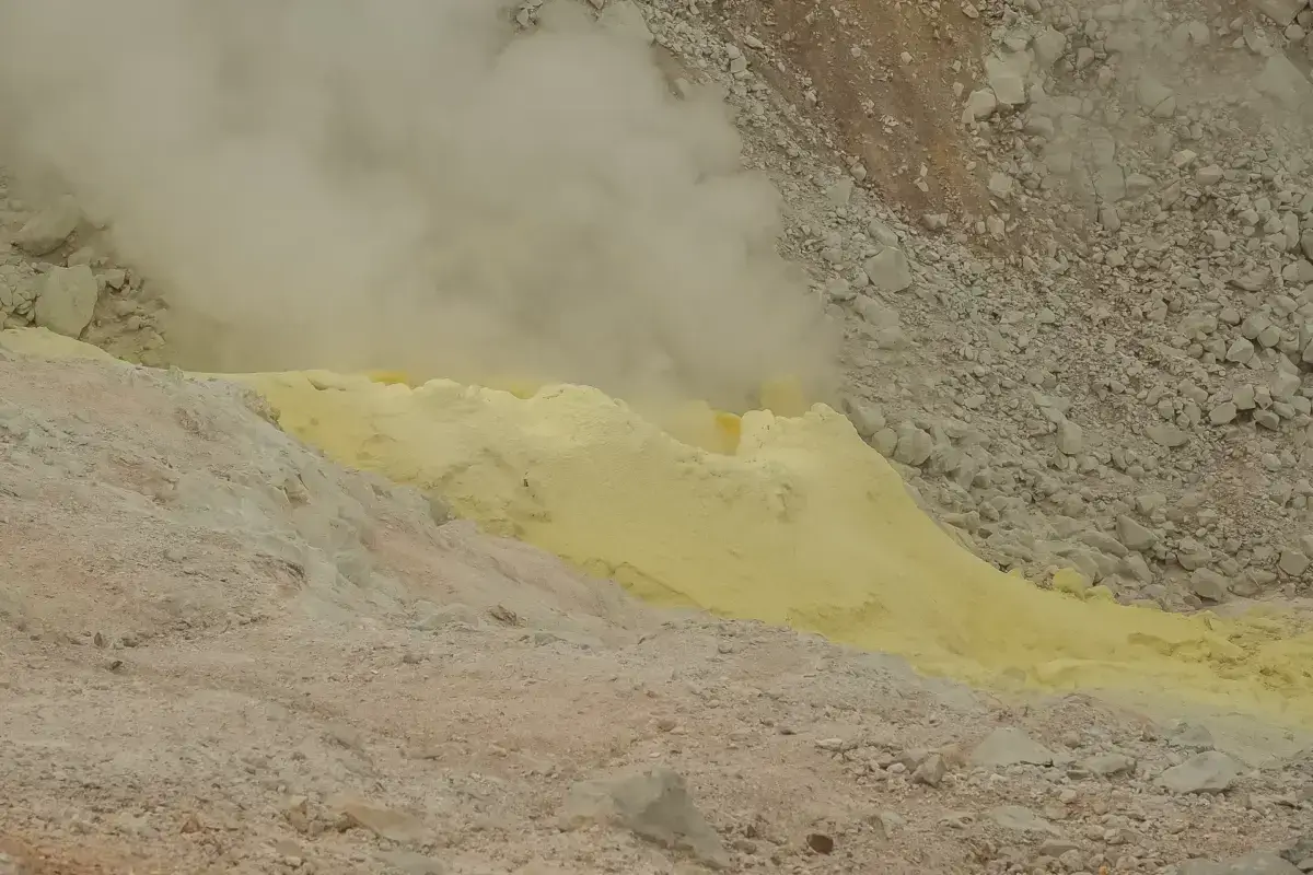 Bright yellow sulfur deposits surrounded by gray volcanic rocks and steam rising from geothermal vents in Teshikaga, Hokkaido.