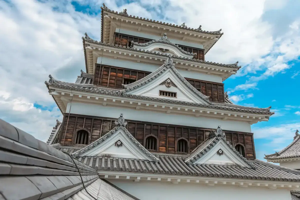 Traditional Japanese castle tower with white walls and distinctive curved tile roofing against a blue sky with scattered clouds, showcasing classic feudal-era architecture.