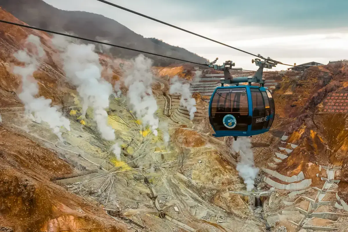 Hakone Ropeway cable car traversing over Owakudani volcanic valley with active sulfur vents and steaming fumaroles below.