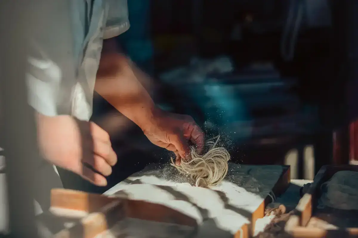 Japanese chef hand-pulling fresh soba noodles with flour dust in mid-air, showcasing traditional noodle-making craftsmanship.