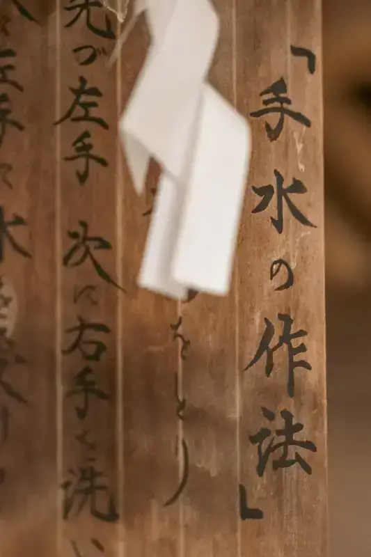 Wooden ema prayer plaques with Japanese calligraphy hanging at a Shinto shrine, with a white paper fortune tied in between.