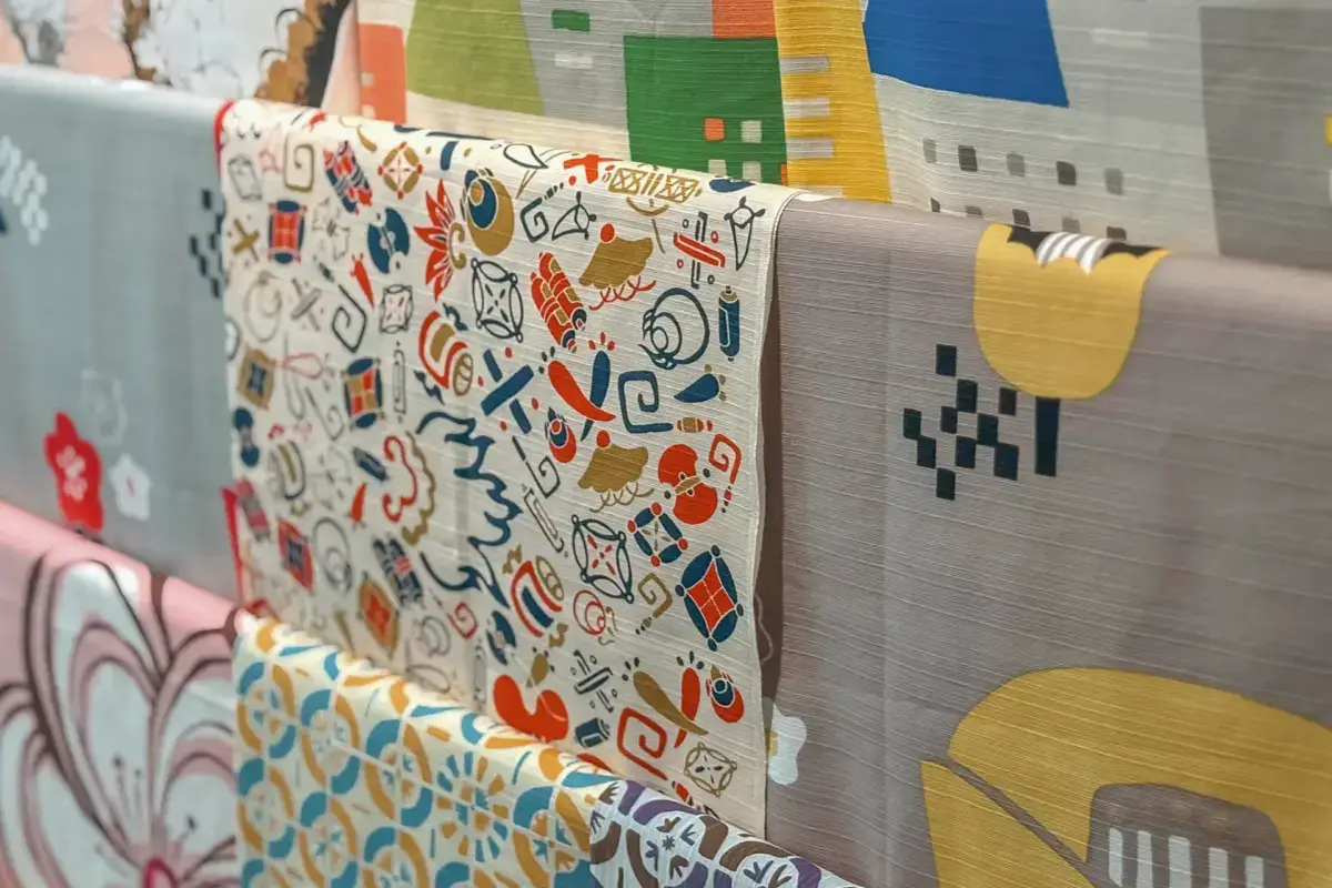 Collection of Japanese textile samples displaying traditional and contemporary patterns including geometric designs, folk motifs, and colorful modern prints arranged on hanging fabric swatches.